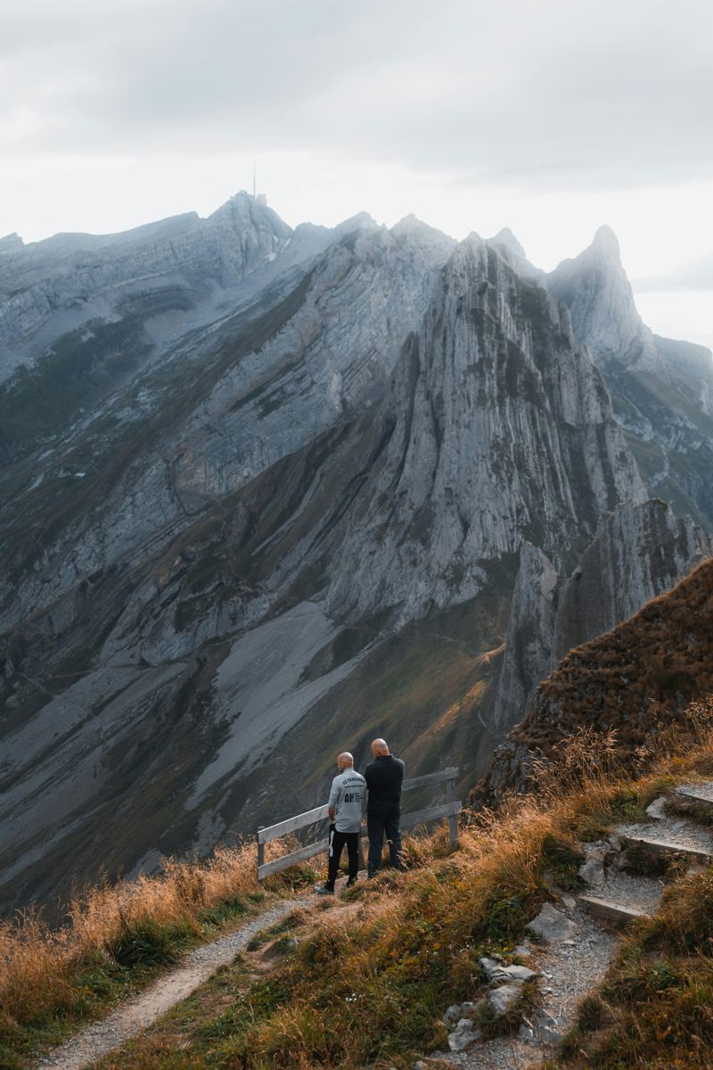 A couple standing on a mountain trail above a valley